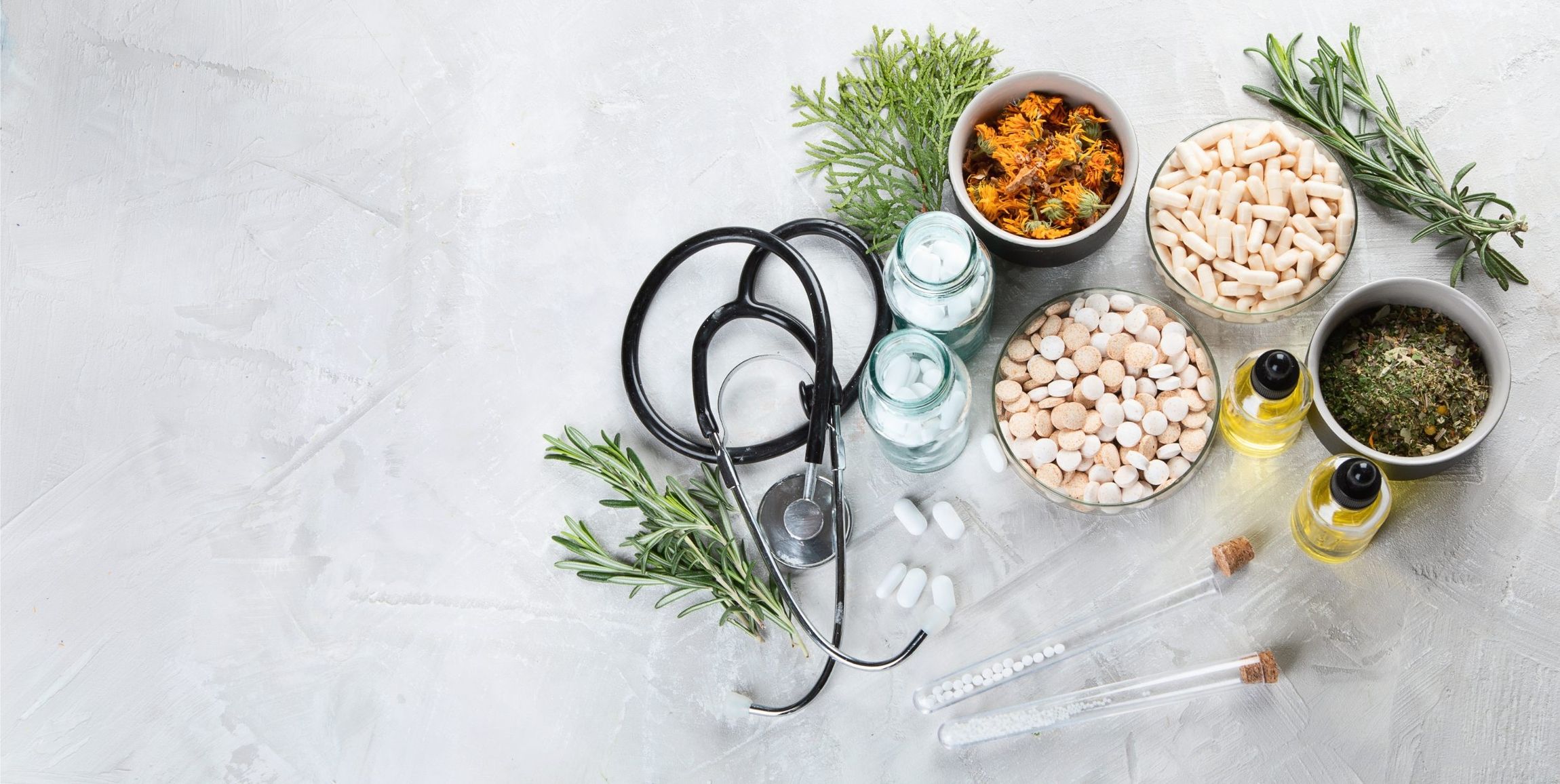 Eine Vielzahl von Kräuterheilmitteln, Nahrungsergänzungsmitteln und ätherischen Ölen, angeordnet mit einem Stethoskop auf einer strukturierten Oberfläche, symbolisiert ganzheitliche Gesundheit.